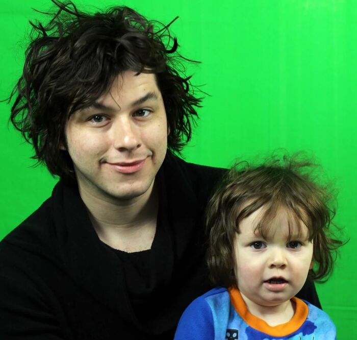 Cameron with wild hair holding toddler Phoenix in front of a green screen